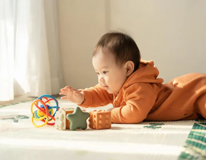 Baby reaching for colorful sensory toys on a warm nursery play mat